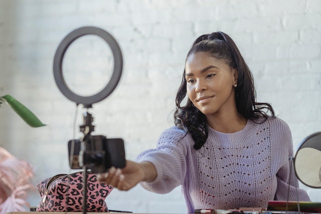 A woman setting up her smartphone in front of a ring light to create a video.