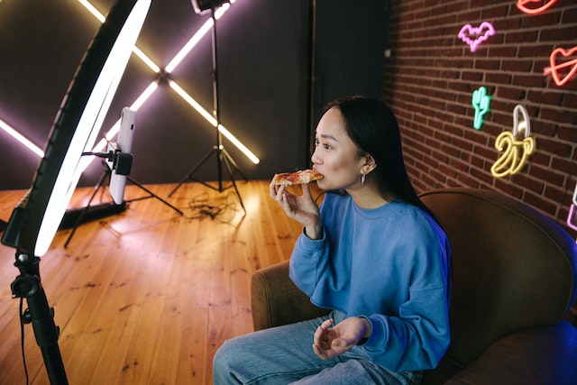Uma garota sentada e comendo pizza enquanto grava um vídeo para o TikTok.