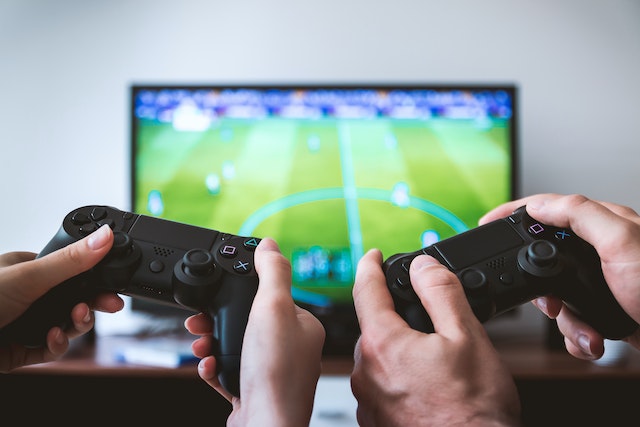 Duas pessoas segurando consoles de jogos em frente a uma TV. 