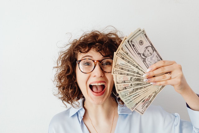 A happy woman in a blue shirt holding money.