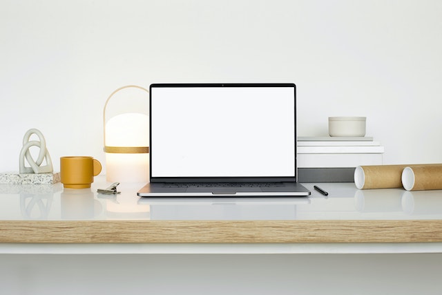 Een MacBook, pen en beker op een wit oppervlak.
