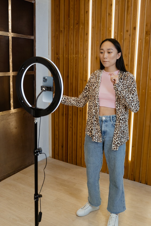 A girl standing and recording a TikTok of herself. 