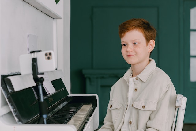 Um garoto gravando um vídeo de si mesmo para o TikTok tocando piano. 