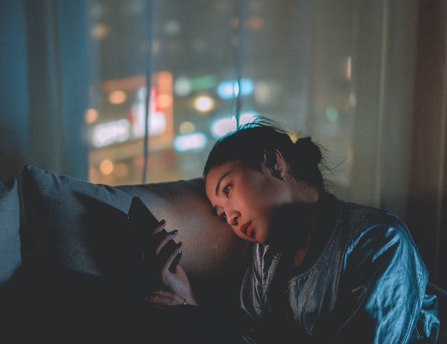 A young lady sitting on a couch and using her mobile phone.