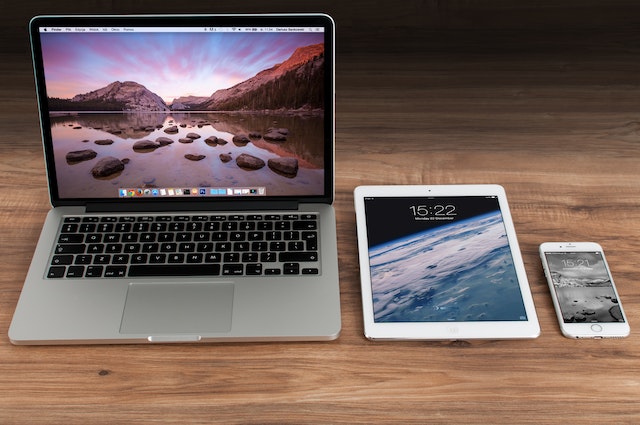 Un iPhone, un iPad și un Macbook pe o suprafață maro.