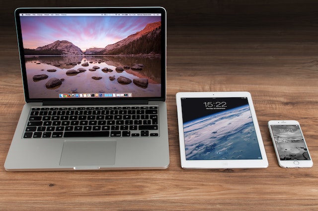 An iPhone, iPad, and a Macbook on a brown surface.