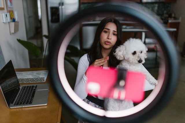 A woman holding her puppy and recording a TikTok.