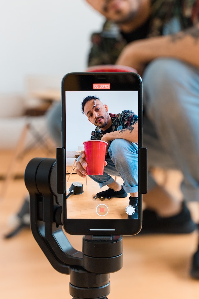 Um homem segurando um copo vermelho e gravando um vídeo de si mesmo para o TikTok.