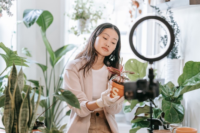A girl holding a plant and recording a TikTok.
