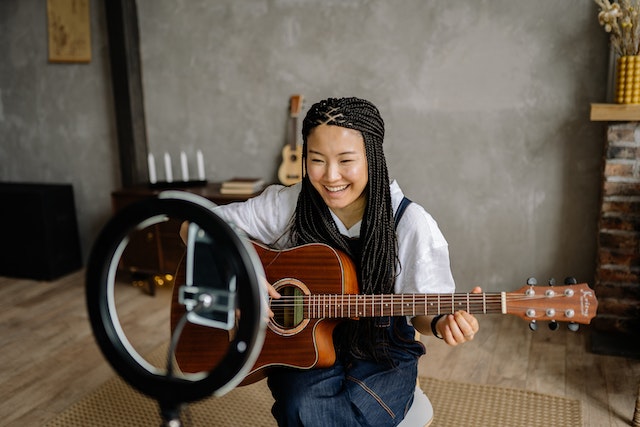 A girl playing the guitar and recording a TikTok.