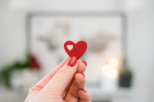 A person holding a small, red, paper heart. 