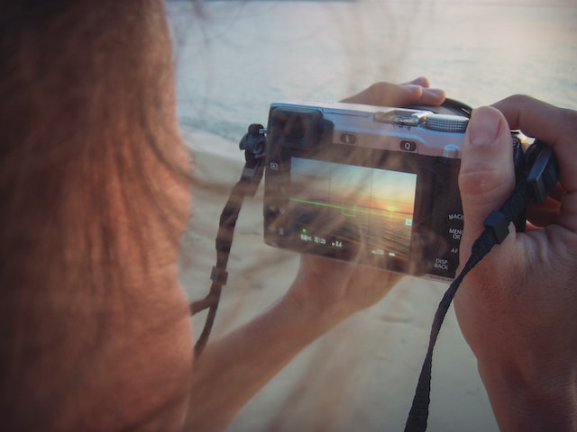 Eine Person, die ein Foto vom Sonnenuntergang am Strand macht.