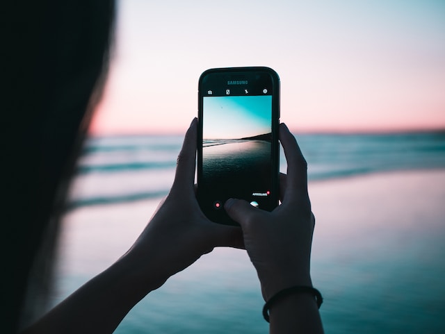 A person taking a video of a beach at sunset.