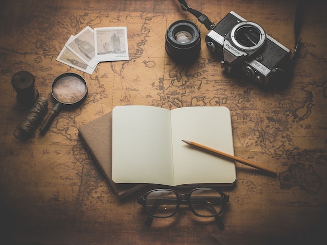 A camera, magnifying glass, journal, and pair of glasses on top of a map.