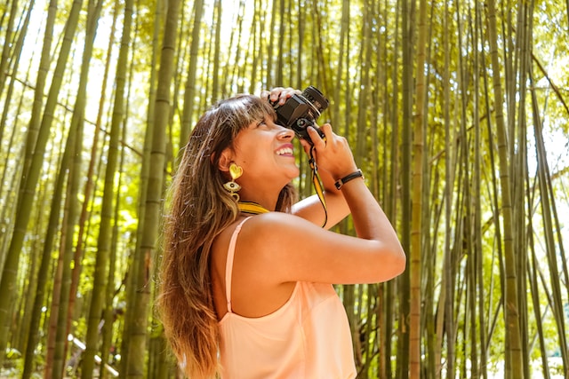 A woman is taking photos of trees with a DSLR camera.