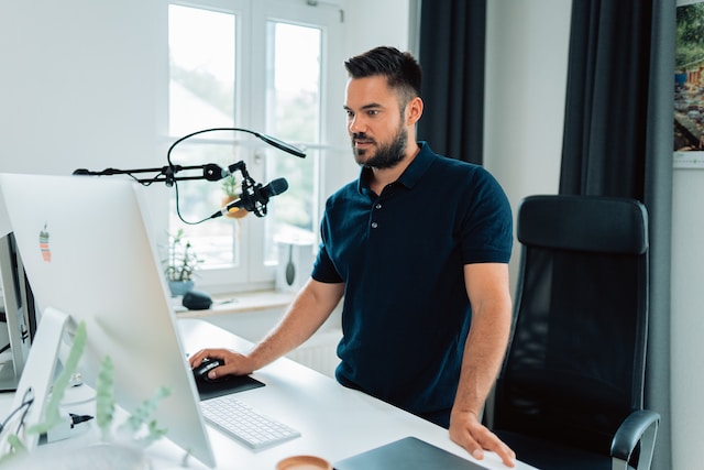 Ein Influencer steht vor seinem Computerbildschirm und seinem Mikrofon.