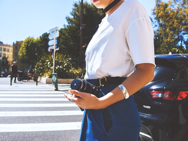 A female traveler carrying a DLSR camera while crossing the street.
