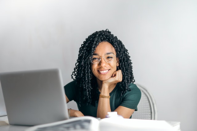 Une jeune influenceuse assise et souriante en train de créer du contenu sur son PC.