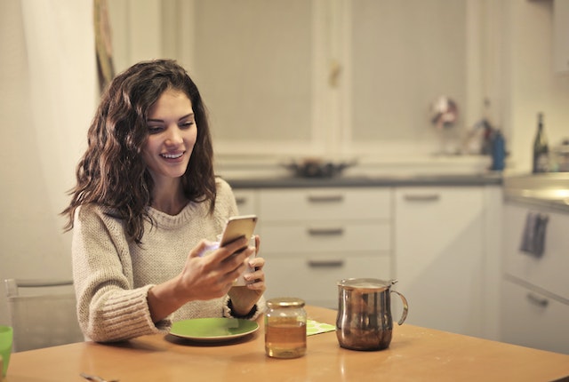 Une femme navigue joyeusement sur l'application TikTok tout en dégustant son repas.