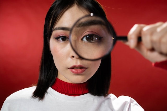 A woman holds a magnifying glass in front of one eye. 