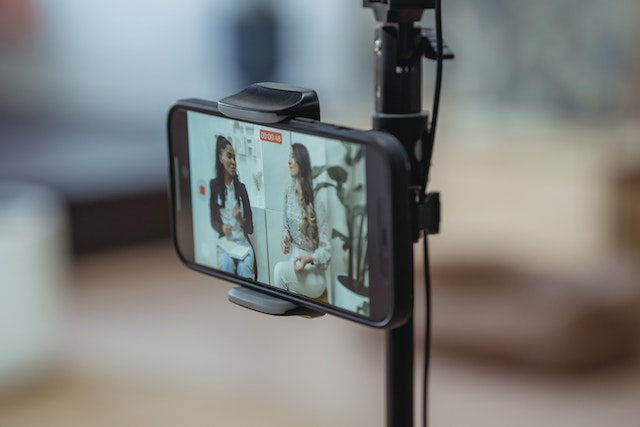 A phone screen displays two women having a discussion while being recorded.