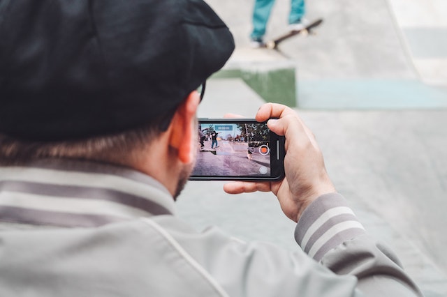 A man sitting and recording a video of people skating for TikTok.