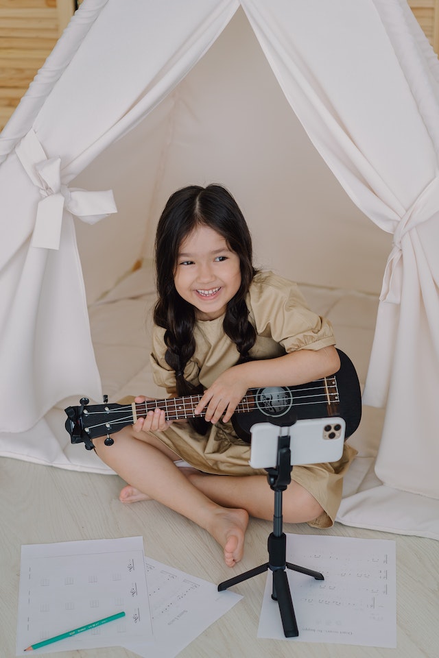 틱톡을 위해 기타로 노래를 연주하는 어린 소녀.