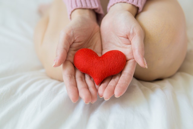 Una donna che tiene il simbolo del cuore tra i palmi delle mani.