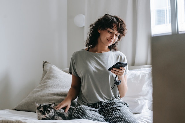 A user sitting on the bed and adding auto-captions to her TikTok videos on her phone.