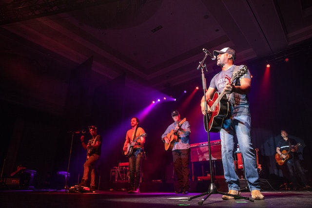 Vijf Amerikaanse countrymuzikanten op een podium in een schemerig verlichte zaal.