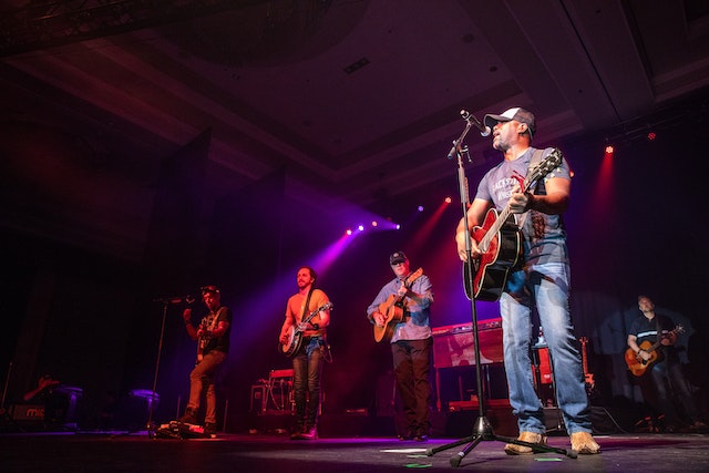 Five USA country musicians on a stage performing at a dimly lit venue.