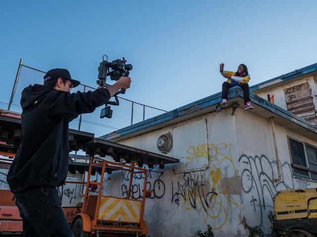 A man filming a person sitting on top of a roof.