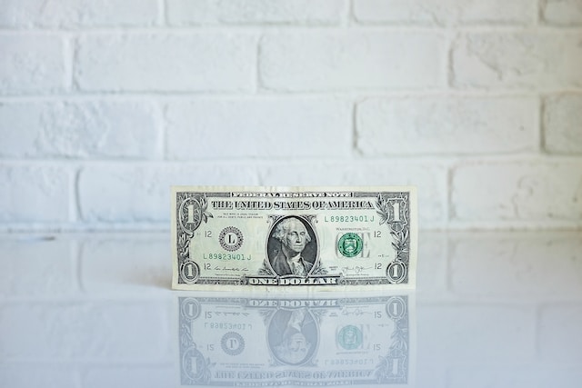 Een foto van één US dollar met een witte bakstenen muur erachter.