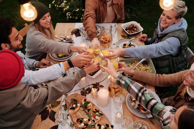 サンクスギビングの料理でいっぱいのテーブルの上で、友人たちが酒を酌み交わしながら乾杯する。 