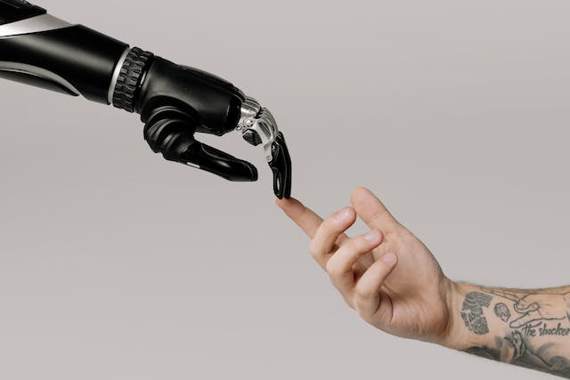 Uma foto mostra uma mão de robô e uma mão humana tocando os dedos. 