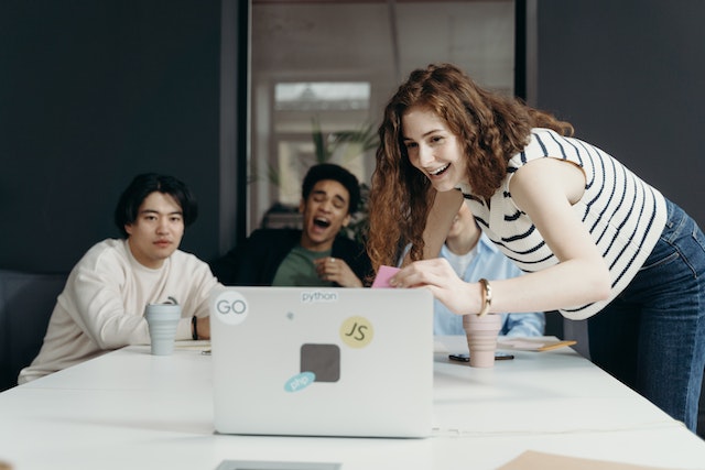 Un grup de prieteni râd la un videoclip pe care îl urmăresc pe un laptop. 