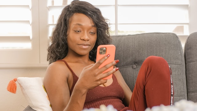 A lady sitting on a couch while she scrolls through TikTok on her phone.