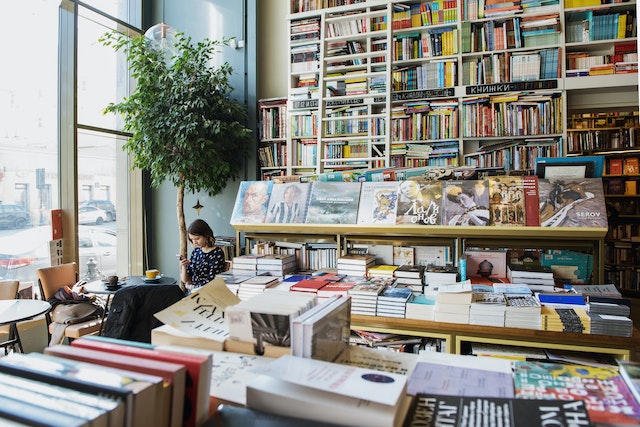  Uma mulher senta-se à mesa de uma livraria enquanto assiste a vídeos em seu celular. 