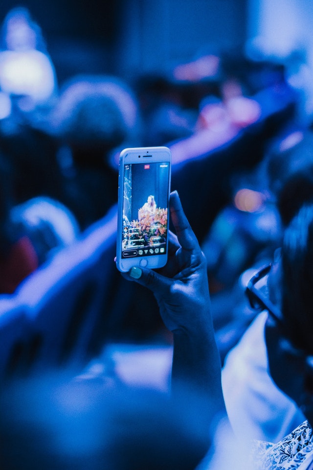 A girl holding a smartphone and recording a concert video for TikTok.
