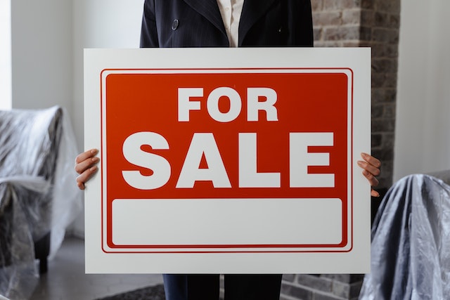 A person holds a red and white For Sale sign.