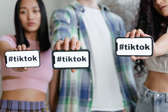 세 명의 크리에이터가 휴대폰 화면에 "TikTok"이라는 단어가 표시된 화면을 보여줍니다.