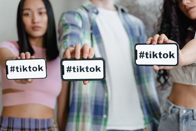 Three people hold up their phone screens displaying the word #TikTok.