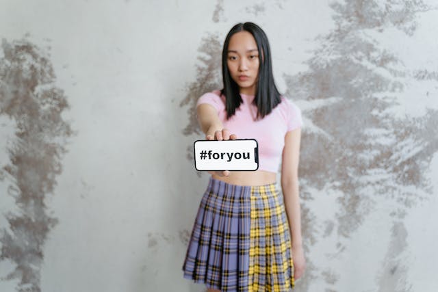  女性が携帯電話を掲げて画面を見せると、そこには "#foryou "と書かれている。