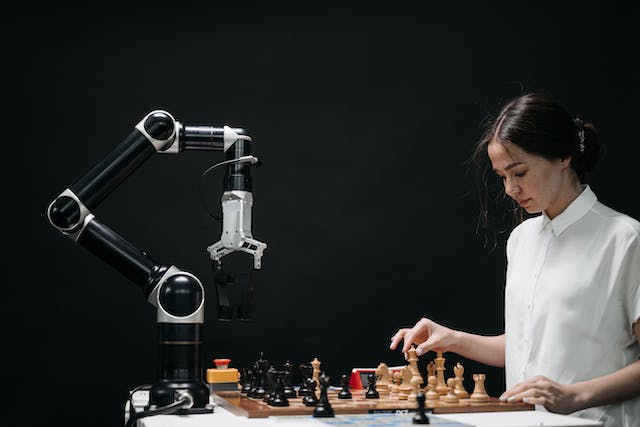 Uma mulher joga xadrez com um robô. 