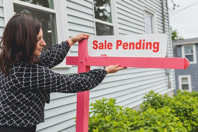 A woman sets up a sign that says, “Sale Pending.”