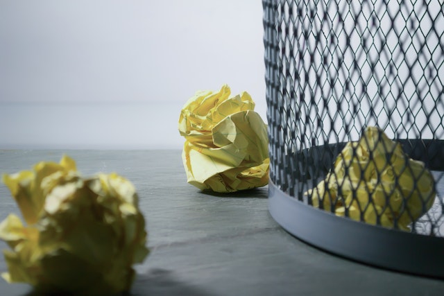 Pieces of crumpled, yellow paper sit in a wire trash bin. 