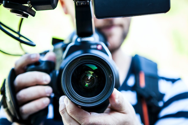 Un prim-plan arată un bărbat care ține în mână un aparat foto DSLR. 