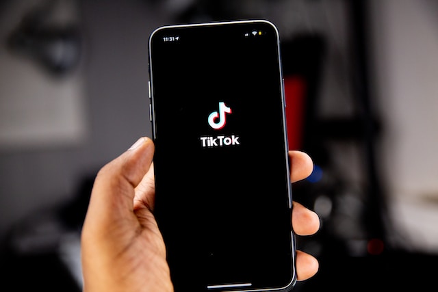 Uma imagem da mão de uma pessoa segurando um iPhone preto que exibe a página de lançamento do aplicativo TikTok.