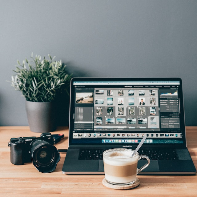 Un'immagine di un computer portatile con diversi modelli di foto, una macchina fotografica a fianco e una tazza di bevanda davanti.