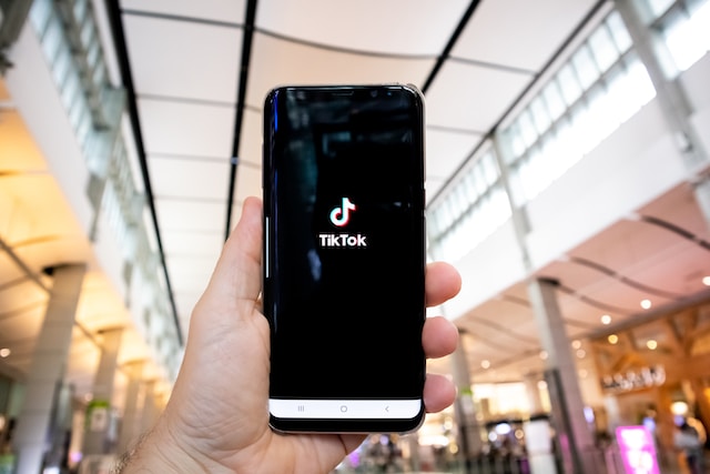 A picture of a hand holding a black smartphone displaying the TikTok app launching page.
